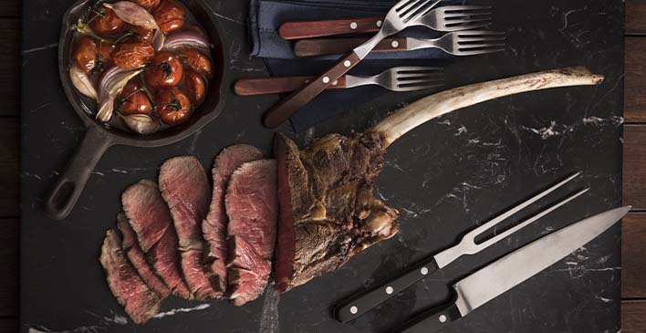 Carne  cortada em cima de uma mesa com garfos e faca do lado