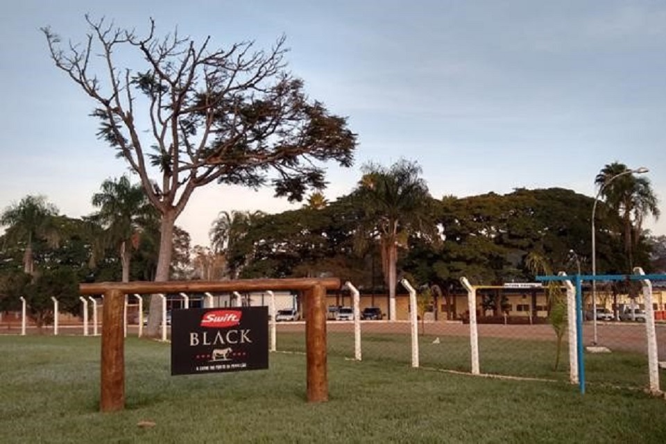 Campo e fazenda com árvores, na frente tem um tronco com uma placa da empresa Swift Black