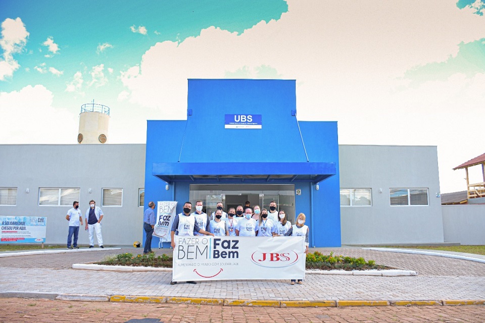 Fachada da UBS de RS na cor azul com pessoas na frente segurando uma faixa do Projeto Fazer o bem Faz Bem JBS.