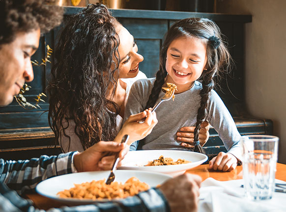 2 adultos e uma criança em uma mesa comendo comida